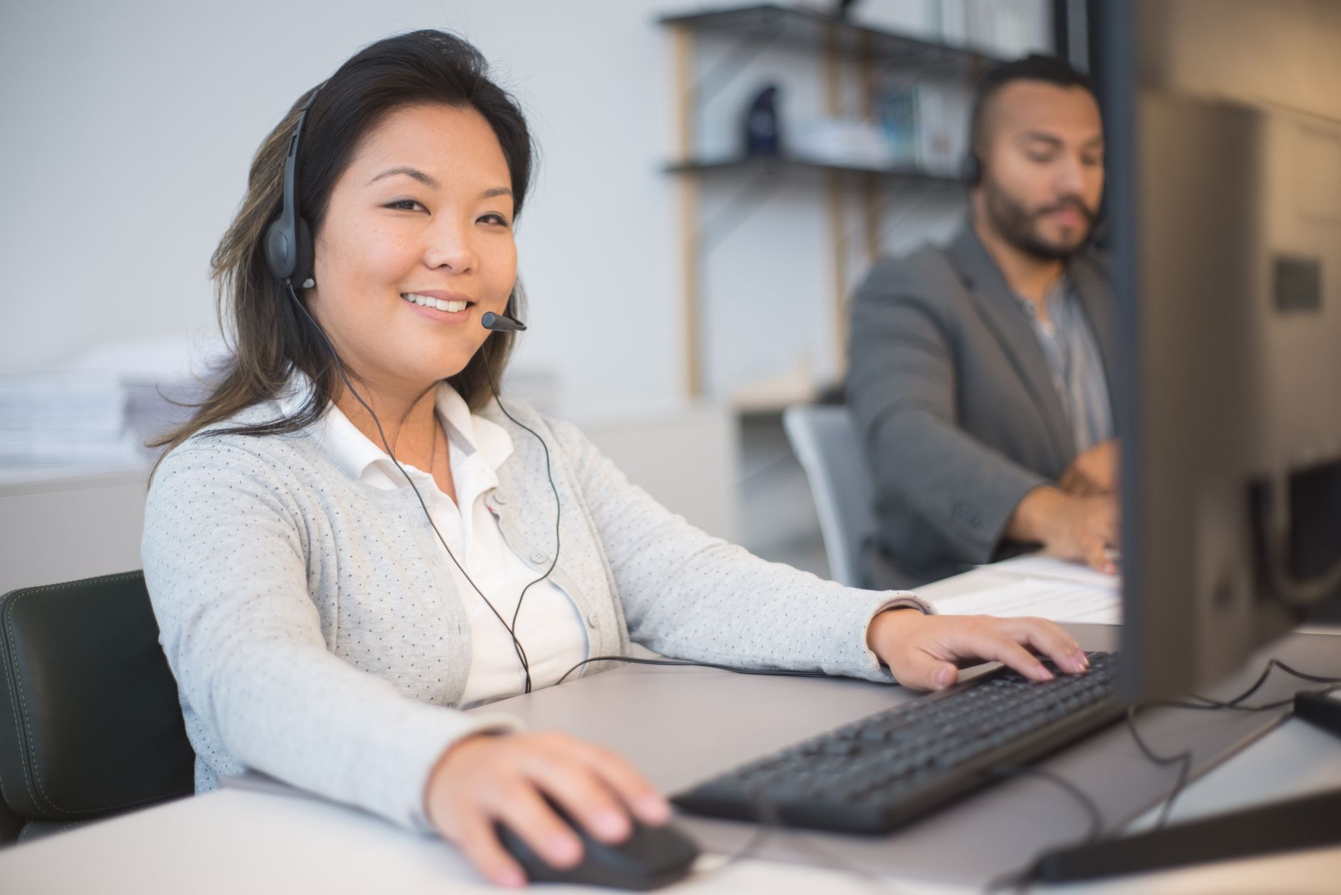 Two call center employees working with headsets in a modern office setting.